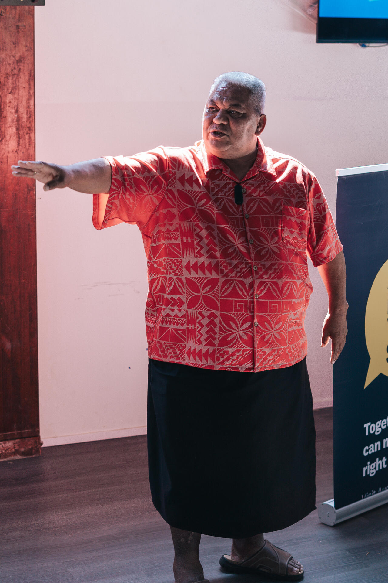 Elder in red shirt speaking passionately at meeting