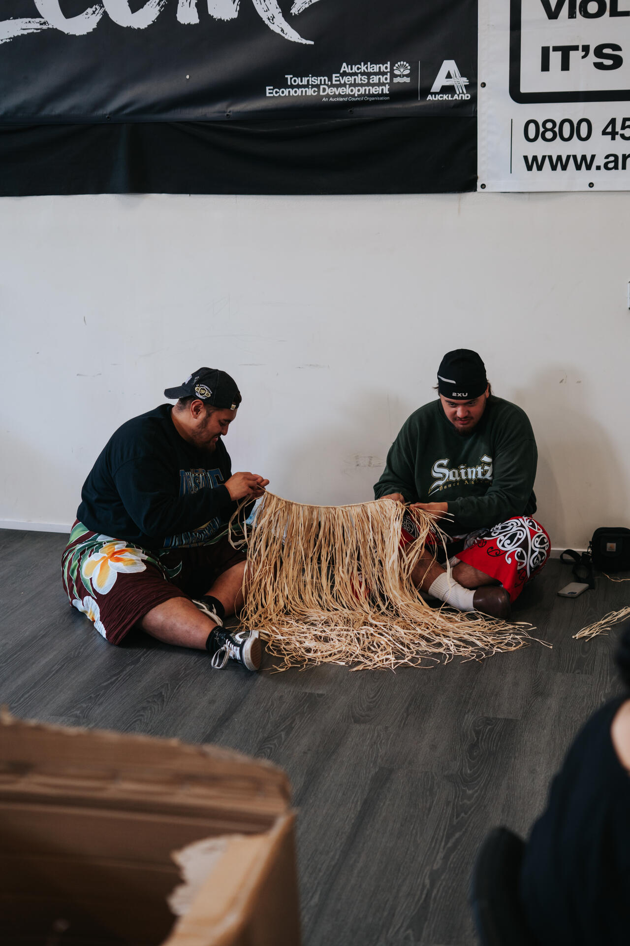 Two men weaving a traditional mat on the floor