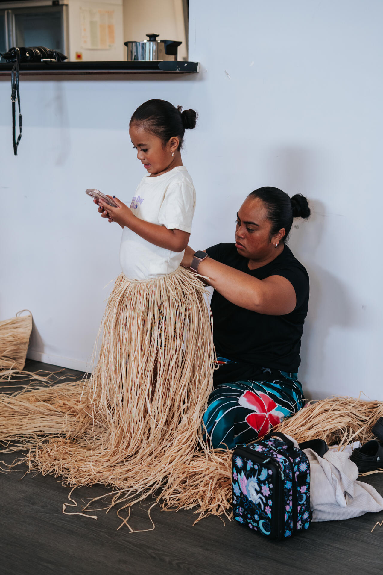 Mother fitting traditional grass skirt on young daughter