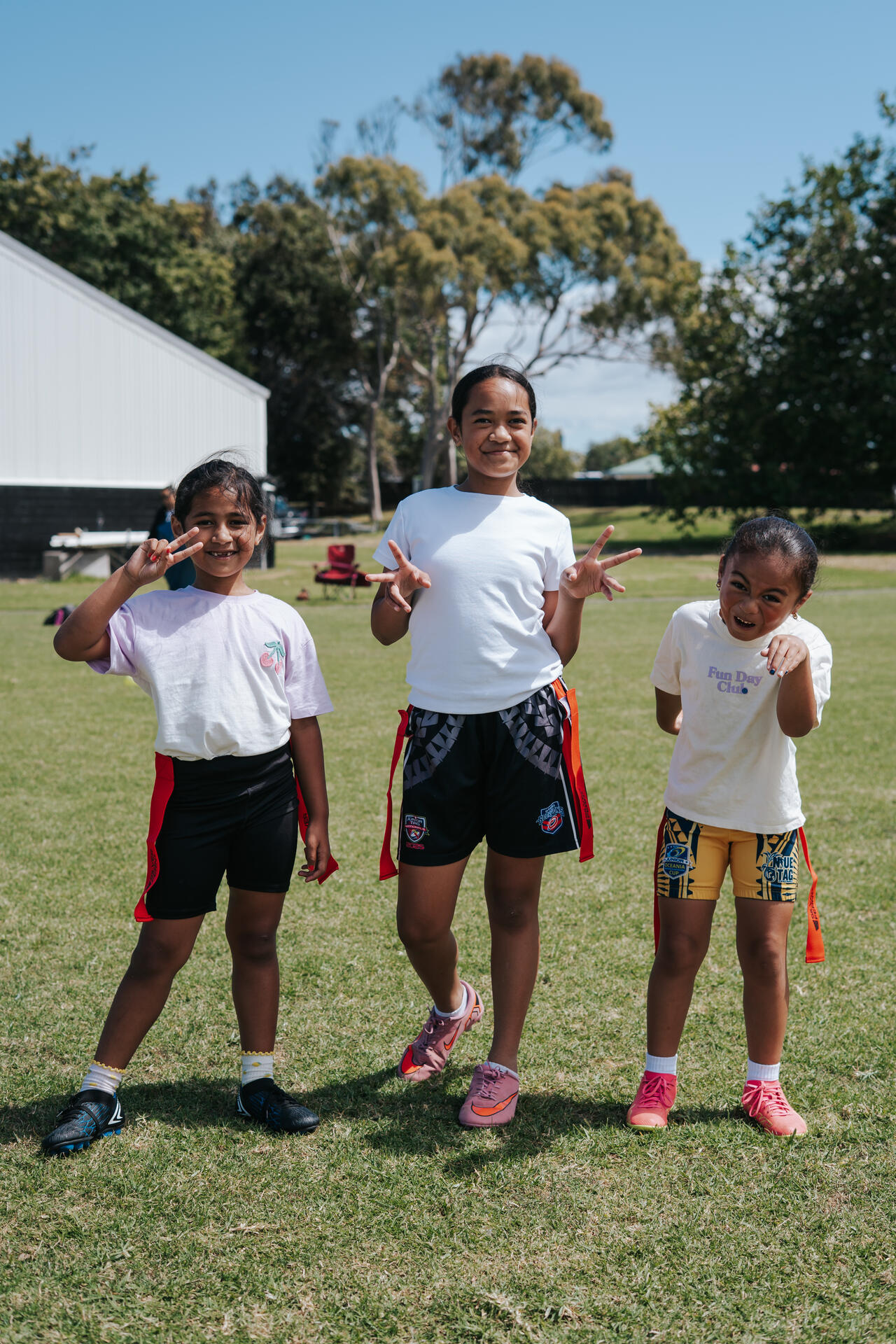 Three young girls posing with peace signs on sports field